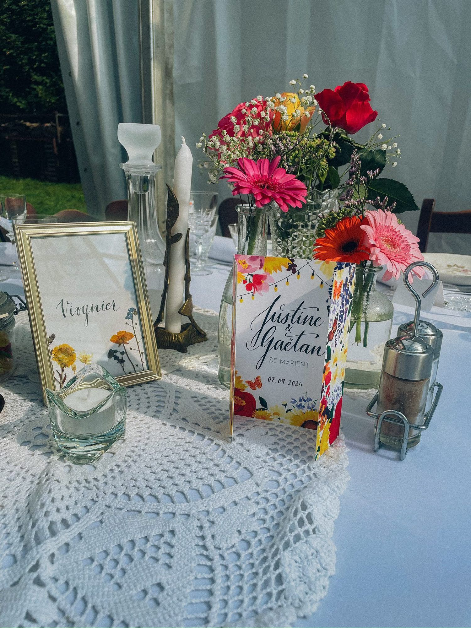 Papeterie de mariage sur une table dressée : menu fleuri « Justine & Gaëtan » et nom de table