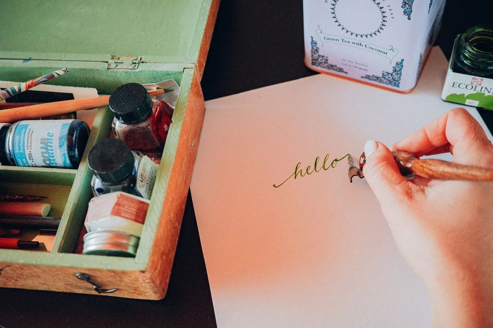 La main de Nora qui calligraphie « hello » à la plume, à côté de sa boîte d'encres